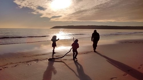 A family playing on the beach at sunset in Tor Bay, Gower
