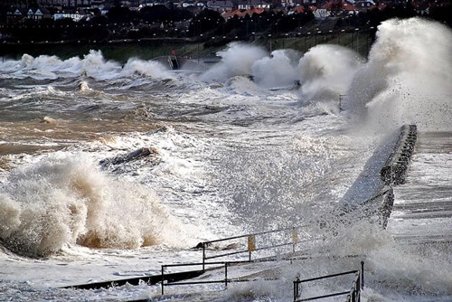 Coastal storm surge at Colwyn Bay with coastal defences visible.