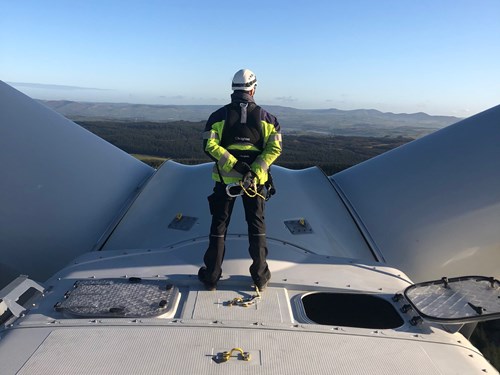 Turbine engineer standing on top of a wind turbine looking out at Welsh landscape